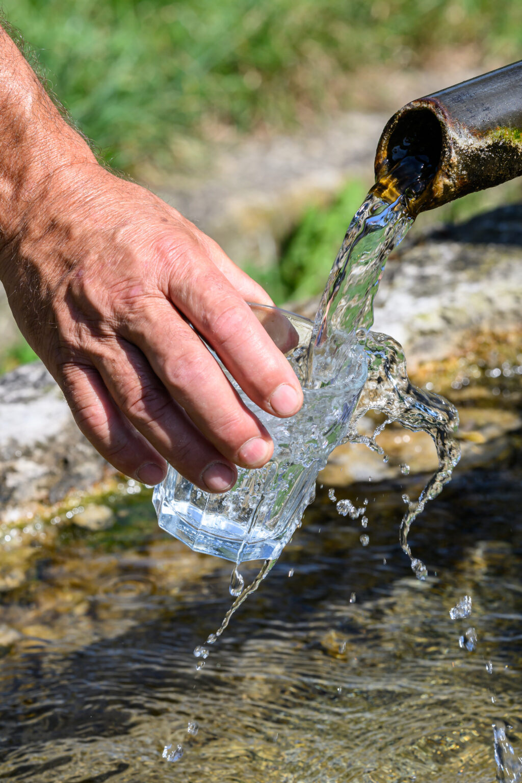 jemand füllt am Brunnen ein Glas mit Wasser